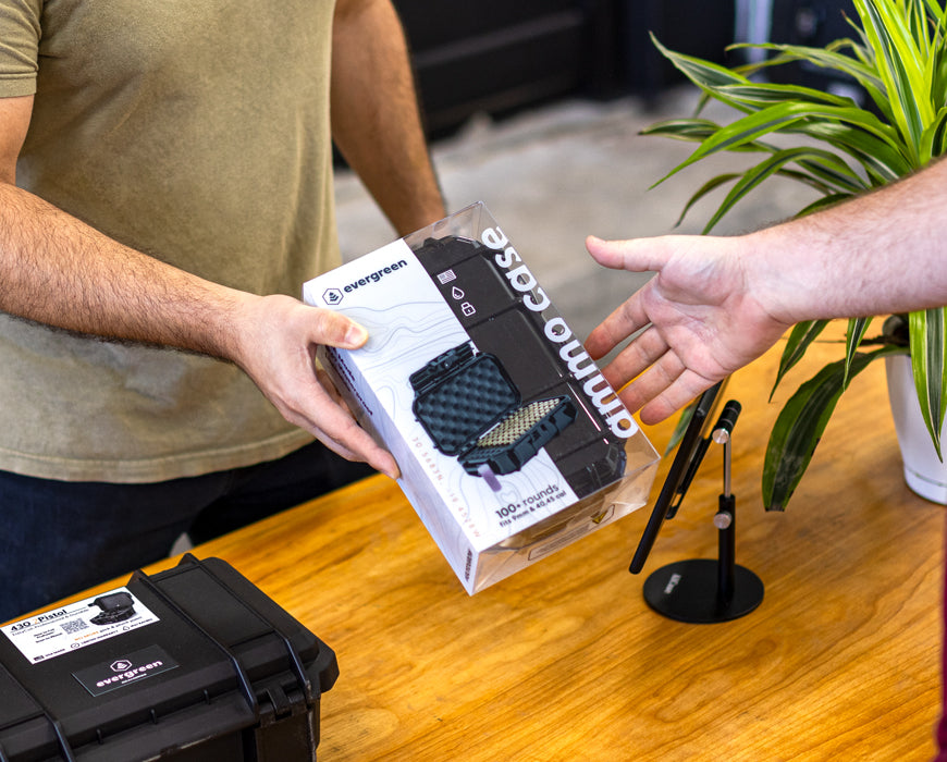 Evergreen ammo case in retail packaging being handed across a table