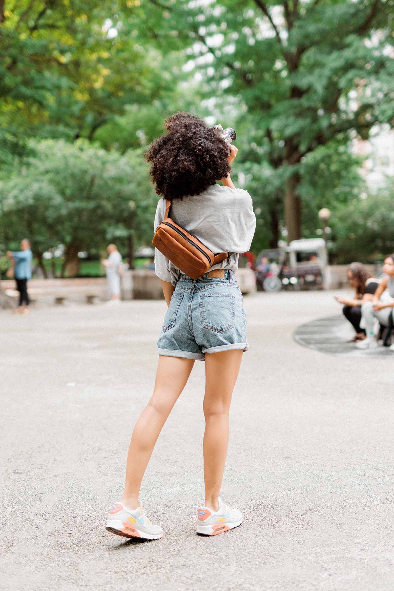 Image of woman taking photo in Central Park with Evergreen Tan Leather Legacy Camera Sling